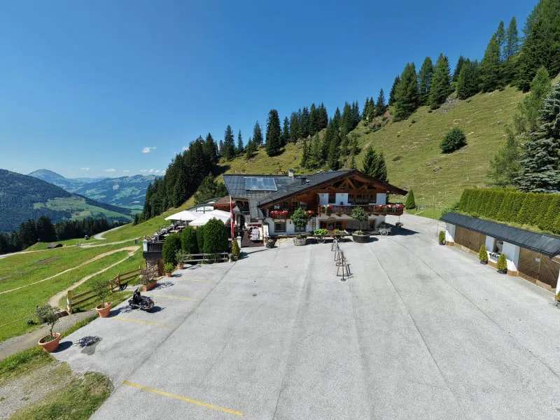 Die OchsAlm aus der Luft, eingebettet in Almwiesen mit Blick über die Kitzbüheler Alpen
