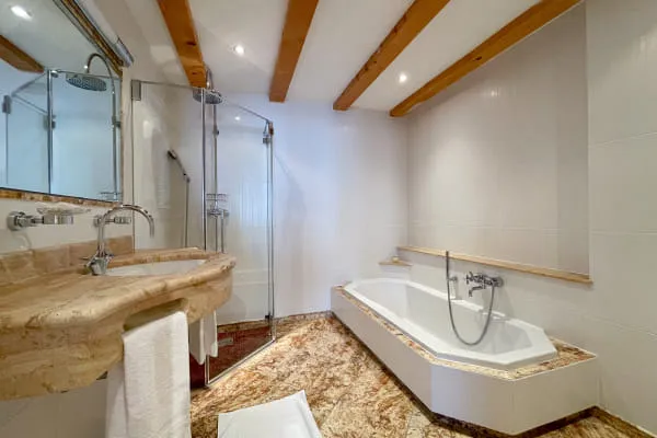 Badezimmer der Suite Ochsalm mit Badewanne, begehbarer Dusche und Waschtisch aus Naturstein